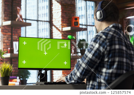 Freelancer listening music, analyzing data on isolated screen PC monitor at desk, compiling analytical reports. Employee wearing headphones using chroma key computer display, finishing project Freelancer listening music, analyzing data on isolated screen PC monitor at desk, compiling analytical reports. Employee wearing headphones using chroma key computer display, finishing project 125857574