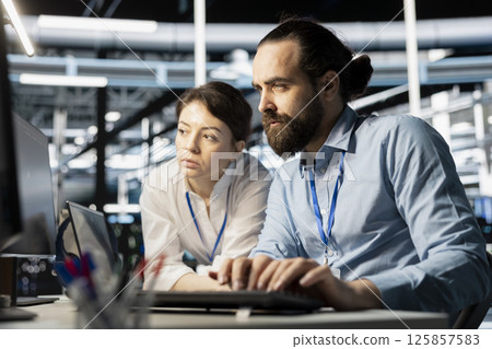Data center coworkers doing brainstorming, running diagnostic scripts on computer, examining hardware. Server room employees talking, working together to evaluate performance metrics 125857583