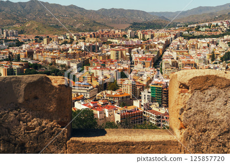 Vibrant cityscape unfolds beyond ancient stone wall under a clear sky. Vibrant cityscape unfolds beyond ancient stone wall under a clear sky. 125857720