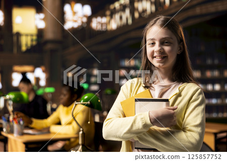 Portrait of preteen schoolgirl carries her textbooks in the library, finishing an important school assignment after her classes. Young scholar dies homework with ambition and diligence. Portrait of preteen schoolgirl carries her textbooks in the library, finishing an important school assignment after her classes. Young scholar dies homework with ambition and diligence. 125857752