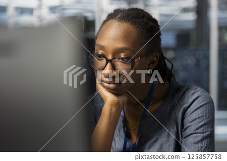 Bored data center technician at work inspecting gear, doing monotonous maintenance tasks. Weary woman in server farm employee conducting system checks to ensure operational stability Bored data center technician at work inspecting gear, doing monotonous maintenance tasks. Weary woman in server farm employee conducting system checks to ensure operational stability 125857758