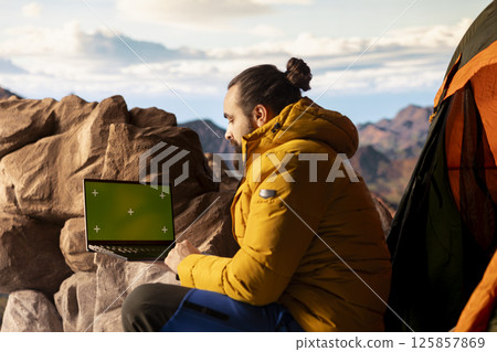 Trekker takes in the panoramic landscape next to isolated mockup screen, where the peaceful mountain scenery and open sky symbolize adventure and perseverance. Wanderlust with tech. Trekker takes in the panoramic landscape next to isolated mockup screen, where the peaceful mountain scenery and open sky symbolize adventure and perseverance. Wanderlust with tech. 125857869