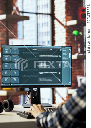 Person seated at desk communicating with AI LLM chatbot software in modern home office. Close up of large language model program interface on computer screen in bright apartment 125857888