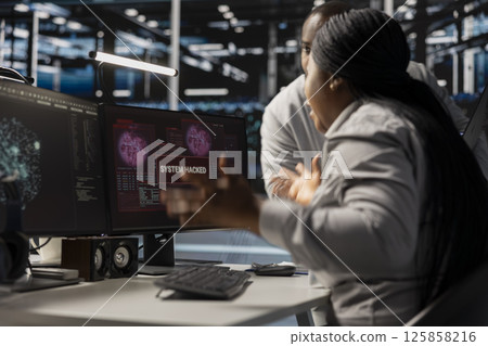 Technicians in data center viewing hacking security breach alert of zero day exploit vulnerability. Cybersecurity colleagues doing brainstorming to trace intrusion origin and apply emergency patches Technicians in data center viewing hacking security breach alert of zero day exploit vulnerability. Cybersecurity colleagues doing brainstorming to trace intrusion origin and apply emergency patches 125858216