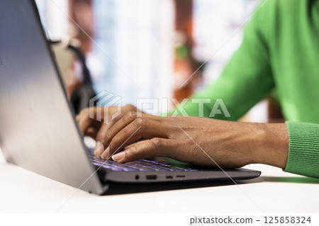 Remote employee seated at home office desk using notebook, checking emails displayed on screen, reading messages in inbox. Close up of teleworker managing electronic correspondence, typing on keyboard 125858324