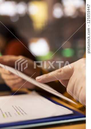 Aged student with a focused expression reading files at college library, academic research and reading textbooks to complete his degree and enrich his understanding of literature. Close up. Aged student with a focused expression reading files at college library, academic research and reading textbooks to complete his degree and enrich his understanding of literature. Close up. 125858447