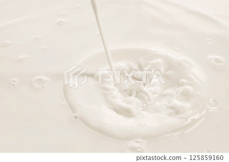 Milk stream hits white liquid creating splash and swirl in soft lighting. 125859160