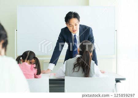 A male teacher teaching children in a classroom 125859297