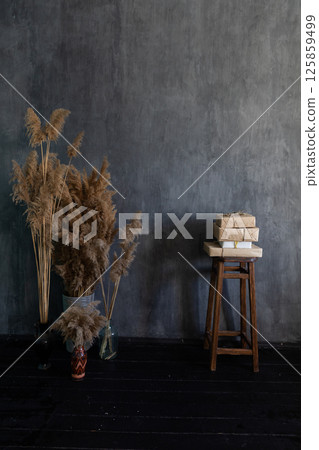 A vase with flowers and a chair with books in the interior of a dark gray room A vase with flowers and a chair with books in the interior of a dark gray room 125859499