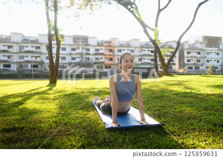 Beautiful woman practicing yoga in cobra pose on mat at a peaceful park 125859631