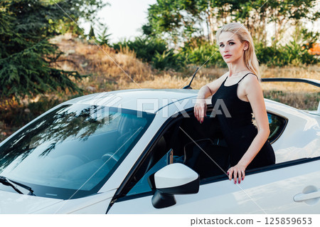 woman in black summer dress at the steering wheel of a sports car 125859653