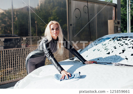 Woman washing white car with foam and water at car wash Woman washing white car with foam and water at car wash 125859661