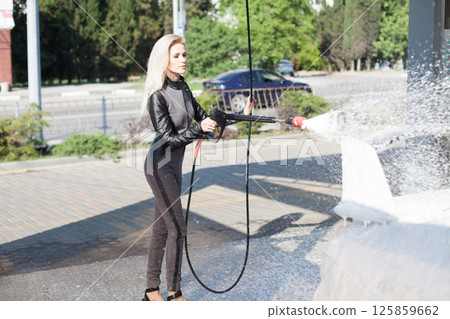 Woman washing white car with foam and water at car wash Woman washing white car with foam and water at car wash 125859662