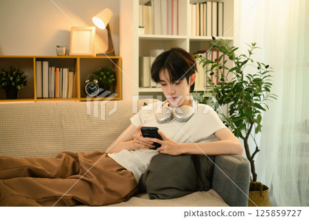 Teenage asian man lying on a sofa and using smartphone in a living room 125859727