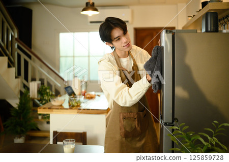 Smiling man doing household chores, cleaning the refrigerator with a cloth 125859728