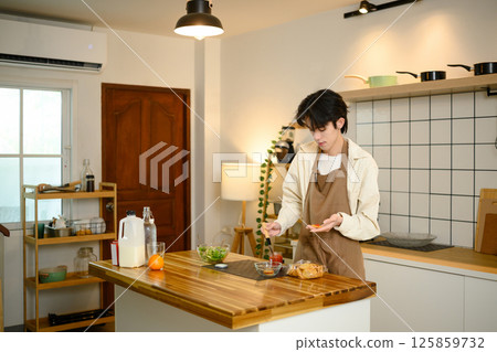 Young man in apron preparing a simple breakfast in a cozy modern kitchen 125859732