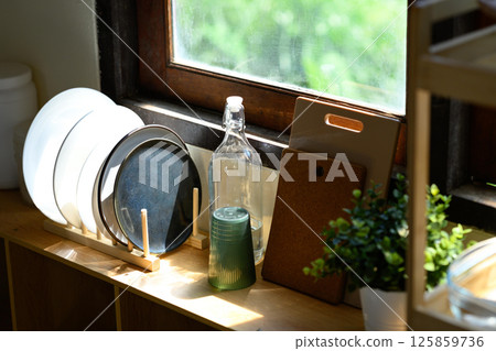 Minimalist kitchen scene with plates, glass bottle, and plant near a wooden window Minimalist kitchen scene with plates, glass bottle, and plant near a wooden window 125859736