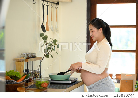 Happy pregnant woman cooking at home preparing a healthy meal in a cozy kitchen 125859744