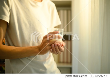 Close up of a man holding a glass of milk while standing indoors in warm natural light 125859745