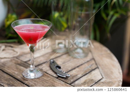Red cocktail with ice in a stemmed glass on a wooden surface Red cocktail with ice in a stemmed glass on a wooden surface 125860641