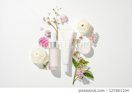 A flat-lay arrangement of cosmetic products in minimalistic packaging surrounded by delicate flowers, highlighting natural beauty and skincare. Lotion bottles, jars, sprays with soft floral decor. 125861104