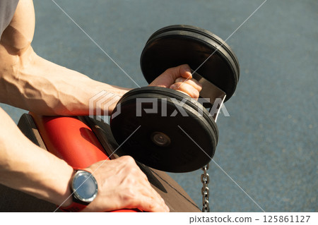 Athlete or bodybuilder training and pump muscular arm with black dumbbell at outside gym. Close up. 125861127