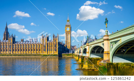 Houses of Parliament and Big Ben rise majestically above the River Thames, with Westminster Bridge creating a picturesque view under a clear blue sky in London. 125861242