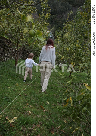 Mother and son walking in green orchard, holding hands Mother and son walking in green orchard, holding hands 125861803