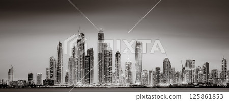 Urban city skyline with illuminated skyscrapers and waterfront railing in black and white at night, Dubai Marina bay UAE 125861853