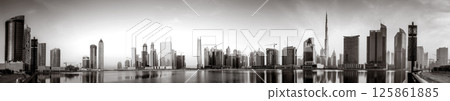 Monochrome city skyline with tall skyscrapers reflecting on calm water under a cloudy sky, Dubai Marina bay UAE 125861885