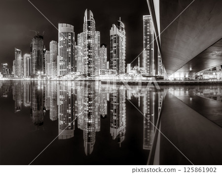 Urban city skyline with illuminated skyscrapers and waterfront railing in black and white at night, Dubai Marina bay UAE Urban city skyline with illuminated skyscrapers and waterfront railing in black and white at night, Dubai Marina bay UAE 125861902