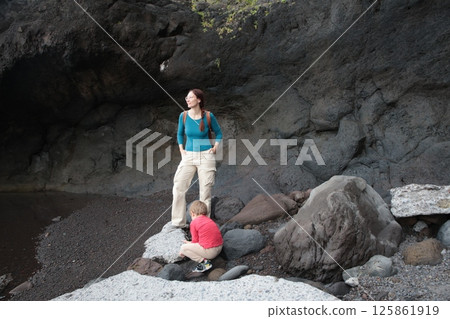 Tourist and child exploring volcanic rocks on beach in canary islands Tourist and child exploring volcanic rocks on beach in canary islands 125861919