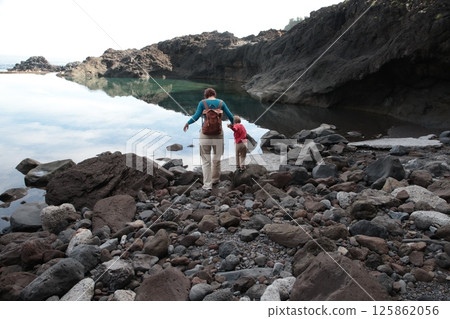 Mother and child exploring rocky coastline on hiking adventure 125862056
