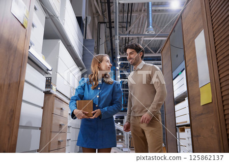 In a modern storage space, a woman and a man chat, highlighting collaboration and innovative design In a modern storage space, a woman and a man chat, highlighting collaboration and innovative design 125862137