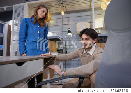 Man and woman engaging in detailed discussion about office furniture features at stylish workspace Man and woman engaging in detailed discussion about office furniture features at stylish workspace 125862168
