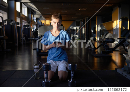 Teen boy with phone searching training video tutorial for sport activity at gym 125862172