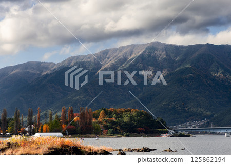 Autumn foliage along the shore of Lake Kawaguchi with colorful trees and mountain slopes Autumn foliage along the shore of Lake Kawaguchi with colorful trees and mountain slopes 125862194