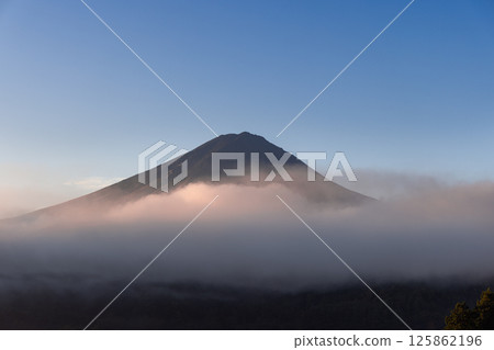 Golden morning light casts a warm glow on the mist surrounding Mount Fuji 125862196