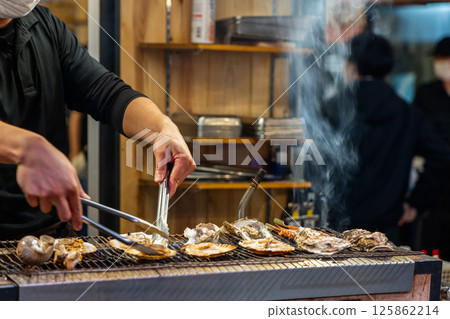 Street food preparation of shellfish on grill in Japan with chef handling fresh oysters and scallops 125862214
