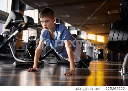 Teenage boy doing push-ups from floor exercising at gym Teenage boy doing push-ups from floor exercising at gym 125862222