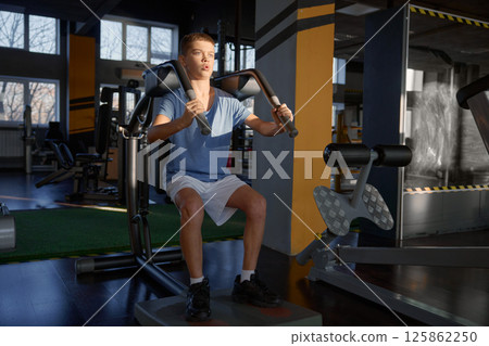 Athletic teenage boy enjoying hard training on fitness machine at gym 125862250