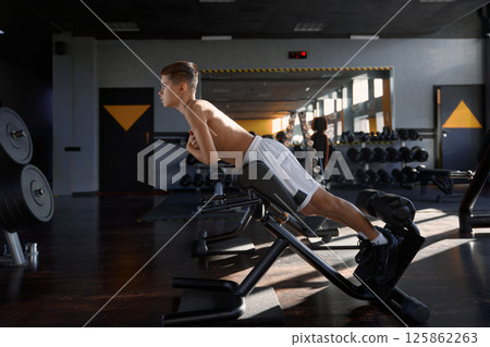 Teenage boy swinging press using special sport equipment at gym 125862263