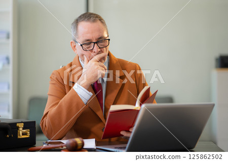 Lawyer middle age is sitting at the pensive reading law table. Lawyer middle age is sitting at the pensive reading law table. 125862502