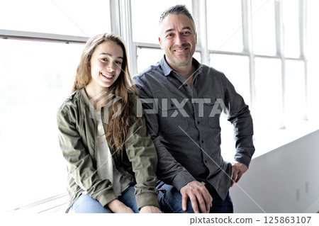 Teenager girl sitting on window with father 125863107