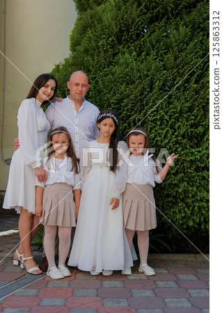 An exquisitely dressed young family. A cute girl in a long white dress and her family. Beautiful young family. 125863312