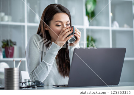 Young woman freezing in cold office, holding warm cup Young woman freezing in cold office, holding warm cup 125863335