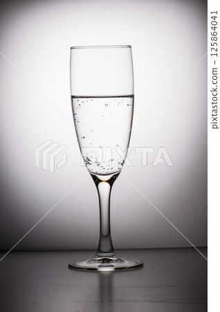 A black-and-white photo depicting a long-stemmed glass. A glass of water. 125864041