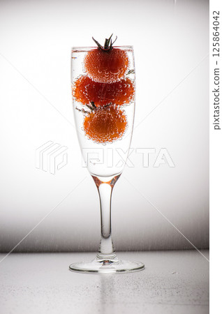 A glass with a stem and three tomatoes in it. A glass with water and three tomatoes in it.  125864042