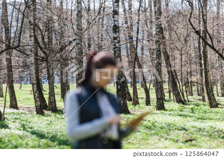 A fashionable lady is walking in a spring park. Blurred foreground. A fashionable lady is walking in a spring park. Blurred foreground. 125864047