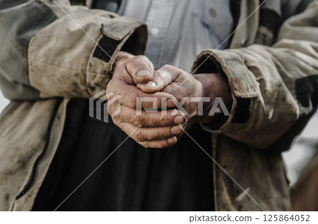 The worker's hands are rough and covered in dirt, showing years of hard labor. His hands bear deep wrinkles and calluses. 125864052